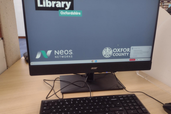 A picture of a computer in a GigaHubs library, with the Neos logo on the screen